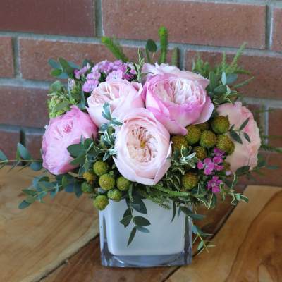 Pink roses arranged in a square glass vase with greenery