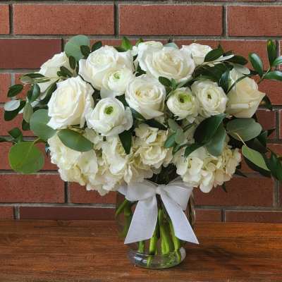 White roses and ranunculus in a glass vase with a white ribbon