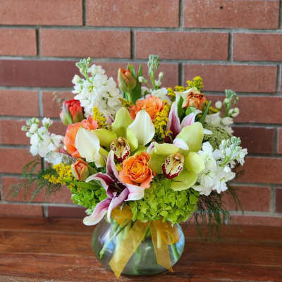 Mixed bouquet in a glass vase with orange roses, orchids, and white blooms