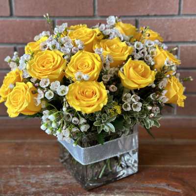 Yellow roses arranged in a square glass vase with small white filler flowers