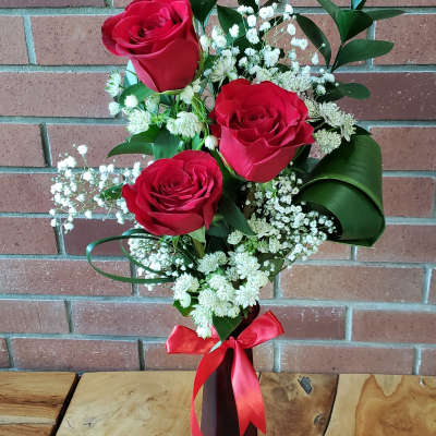 Tall red vase with three red roses and white filler flowers tied with a red ribbon