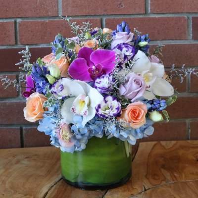 Mixed bouquet of orchids, roses, and hydrangeas in a green glass vase