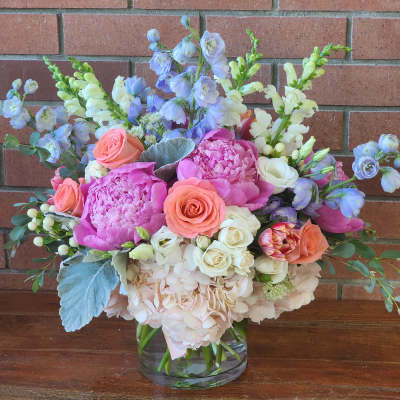 Mixed bouquet of pink, peach, white, and blue flowers in a glass vase