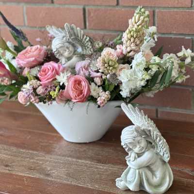Pink and white floral arrangement in a white bowl with angel figurines