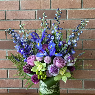 Blue iris and purple flowers in a green glass vase