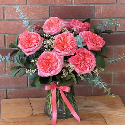Pink roses in a glass vase with eucalyptus and a pink ribbon