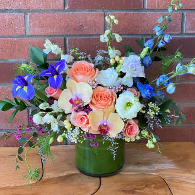 Mixed bouquet in a green glass vase with peach roses and blue irises