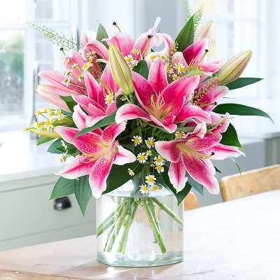 Pink lilies and small white daisies arranged in a clear glass vase