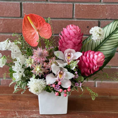 Tropical floral arrangement in a white square vase with pink and white blooms