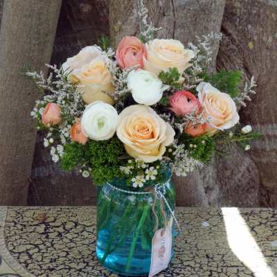 Peach and white roses with ranunculus and filler flowers arranged in a blue glass mason jar