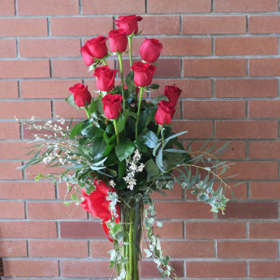 Tall vase arrangement of red roses with trailing greenery