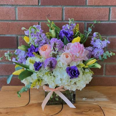 Bouquet of pink, purple, and yellow flowers in a glass vase with a ribbon