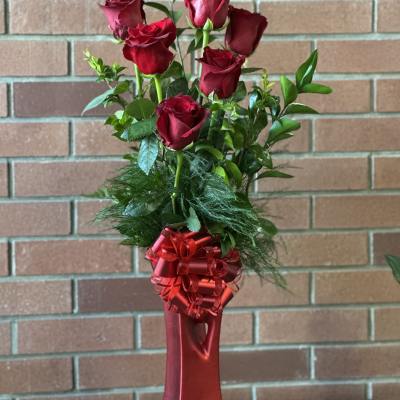 Red roses in a tall red vase with a ribbon bow