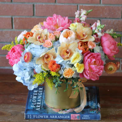 Colorful mixed flower arrangement in a gold vase on stacked books