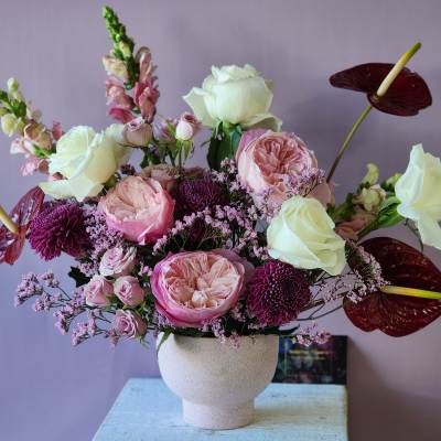 Pink and white floral arrangement in a white vase with burgundy anthuriums