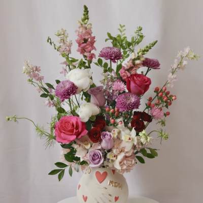 Mixed pink and white flower arrangement in a cream vase with heart decorations
