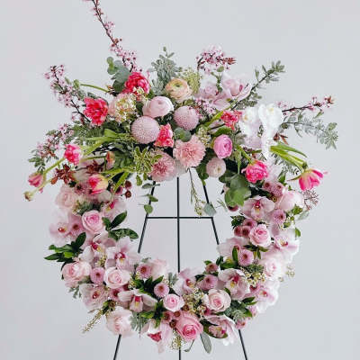 Pink floral wreath on a black stand with roses and orchids