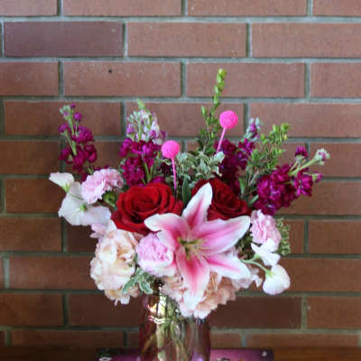 Pink and red floral arrangement in a glass vase on a book box