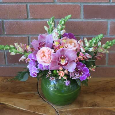Pink and purple flowers arranged in a green glass vase