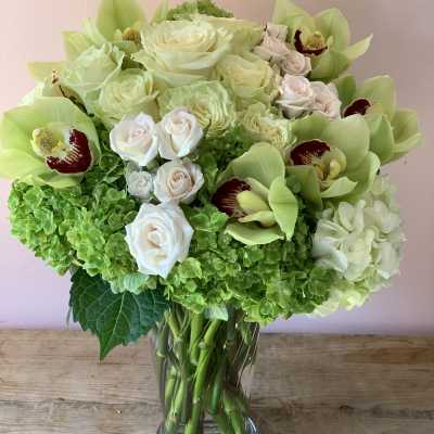 Bouquet of pale roses, green orchids, and hydrangeas in a glass vase