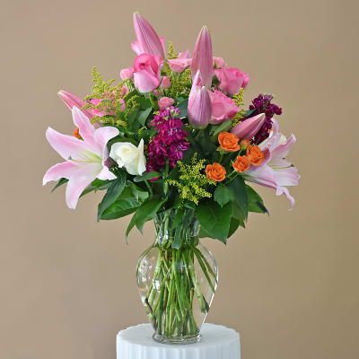 Pink lilies and roses arranged in a clear glass vase