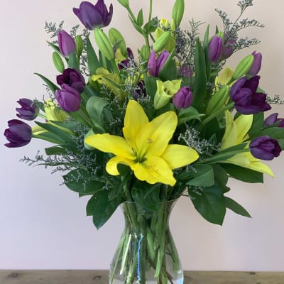 Bouquet of yellow lilies and purple tulips in a clear glass vase