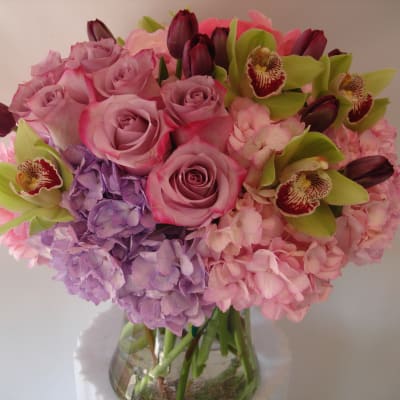 Pink and lavender bouquet with roses, hydrangeas, and orchids in a glass vase