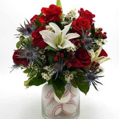 Red roses and a white lily in a glass vase filled with baseballs
