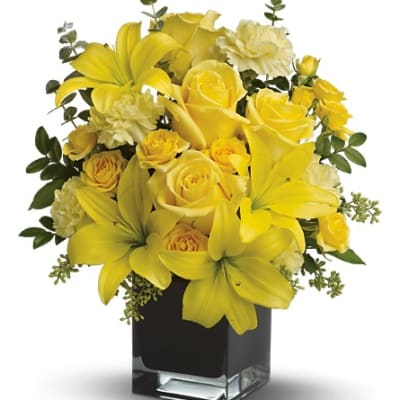 Yellow roses and lilies arranged in a square glass vase
