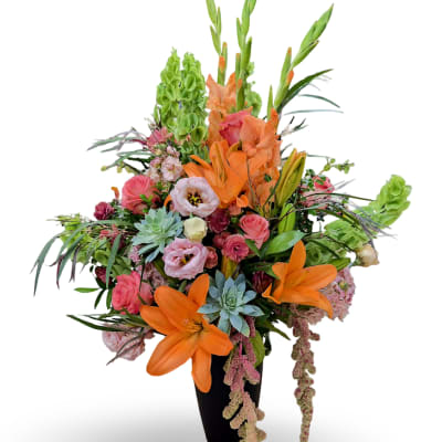 Tall mixed bouquet with orange lilies, pink roses, and green blooms in a black vase