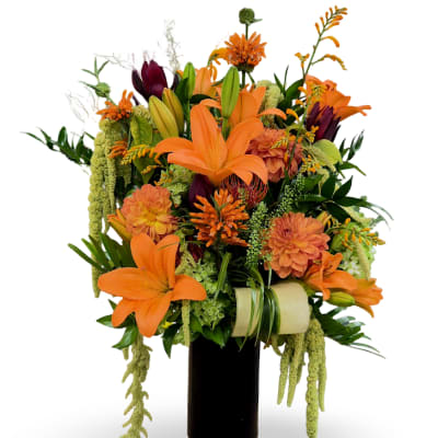 Orange lilies and mixed flowers arranged in a tall black vase