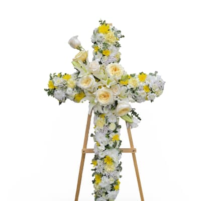 Cross-shaped floral tribute on a wooden easel with white and yellow flowers