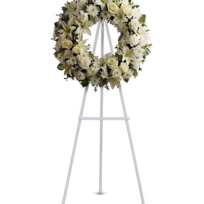 White floral wreath of roses, lilies, and mums on a tall white easel stand
