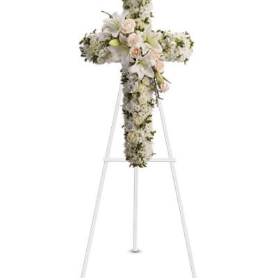 Standing cross of white flowers with lilies and pale roses on a white easel