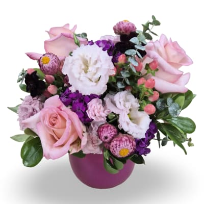 Pink roses and white blooms arranged in a purple vase