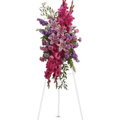 Tall pink and purple standing spray with lilies, roses, and gladiolus on a white easel.