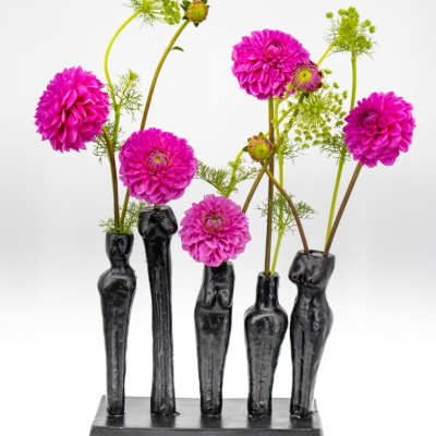 Five magenta flowers arranged in black sculptural vases on a rectangular base.