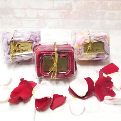 Three clear gift boxes of rose petals tied with gold ribbon.