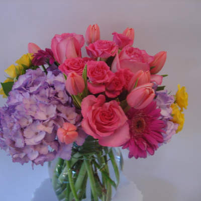Mixed bouquet of pink roses, tulips, hydrangeas, and a gerbera daisy in a glass vase