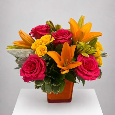 Bouquet of pink roses, yellow spray roses, and orange lilies in an amber vase