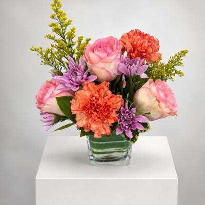 Pink roses, orange carnations, and purple daisies in a glass vase