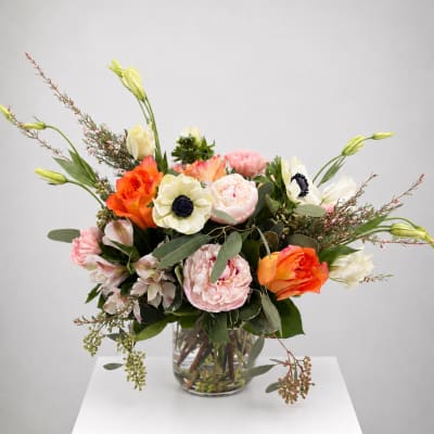 Mixed bouquet of orange, pink, and white flowers in a clear glass vase