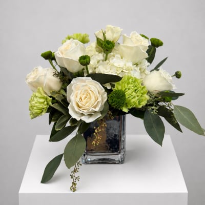 White roses and green carnations arranged in a clear square vase