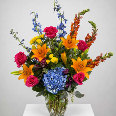 Bright mixed bouquet with roses, lilies, hydrangea, and blue delphinium in a glass vase