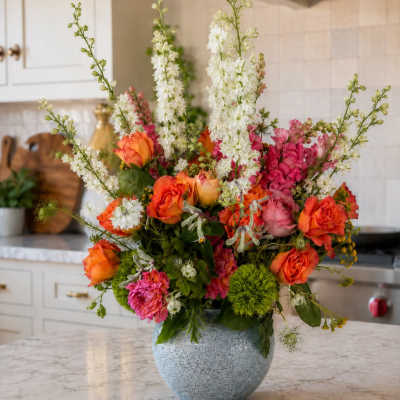 Colorful bouquet of orange roses, pink blooms, and white spikes in a blue vase