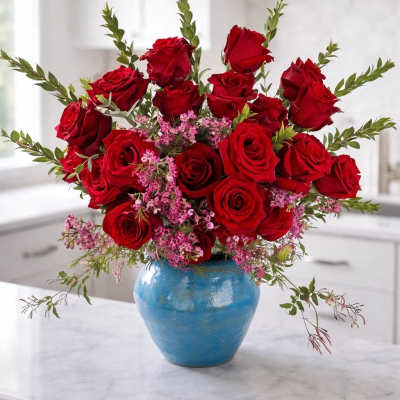 Red roses arranged in a blue vase with pink filler flowers