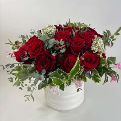 Red roses arranged in a white vase with mixed greenery and small pink accents
