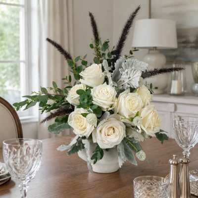 White rose arrangement in a low vase with greenery and dark feathery accents