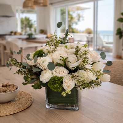 White rose arrangement in a square glass vase with green accents