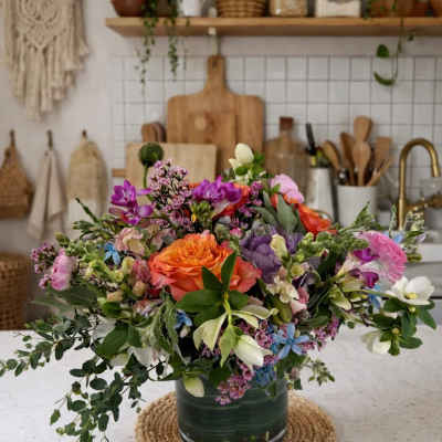 Mixed bouquet of orange, pink, purple, and white flowers in a glass vase